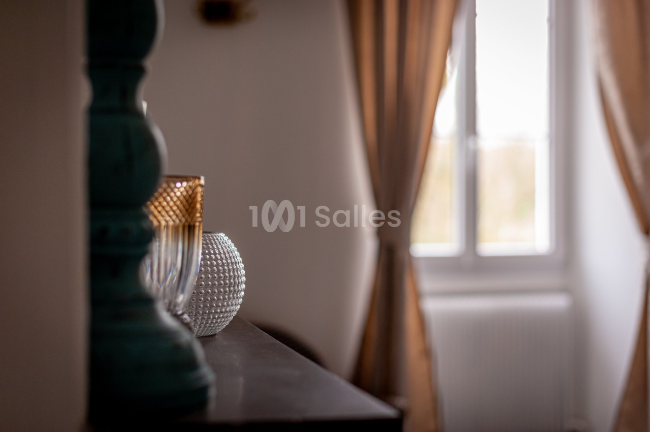 Un intérieur lumineux avec une fenêtre voilée, des rideaux beige et des objets décoratifs sur un meuble sombre.