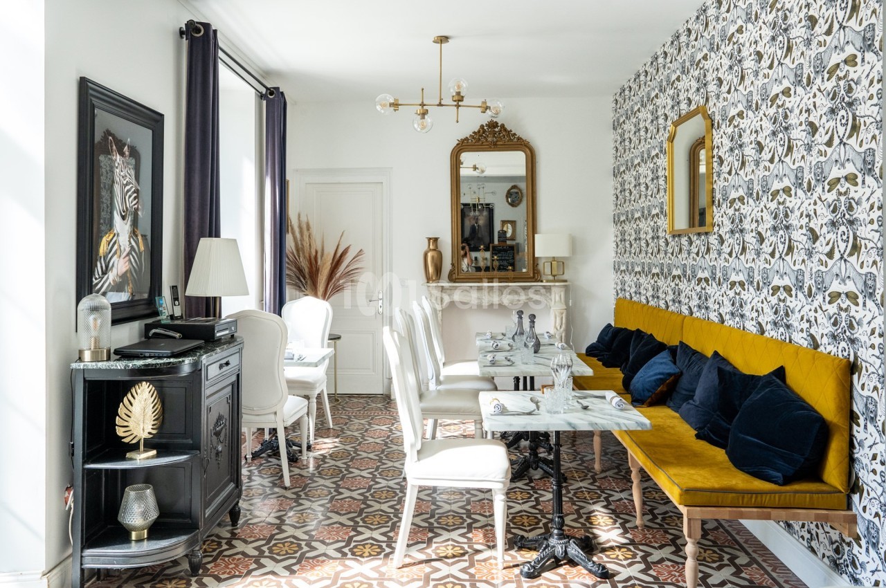 Salle à manger lumineuse avec banquette jaune, chaises blanches, tables en marbre et décoration murale à motifs.