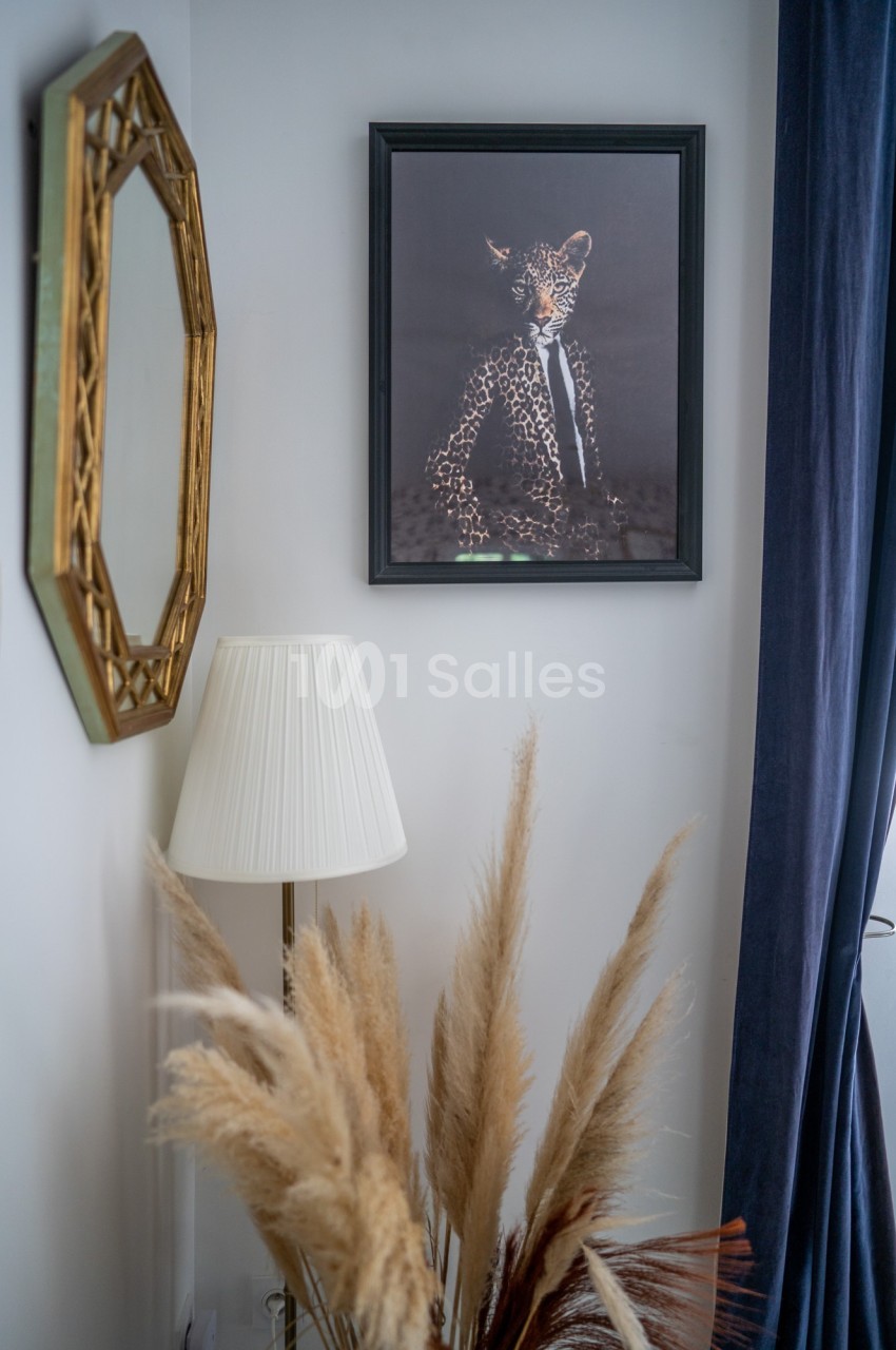 Table de chevet avec lampe, miroir doré, tableau d'un léopard en costume et bouquet de pampas dans un coin de pièce.