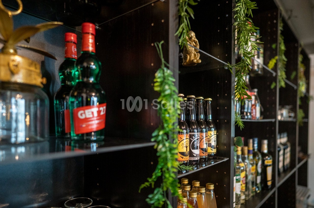 Étagères noires garnies de bouteilles d'alcool variées et décorées de plantes vertes suspendues.
