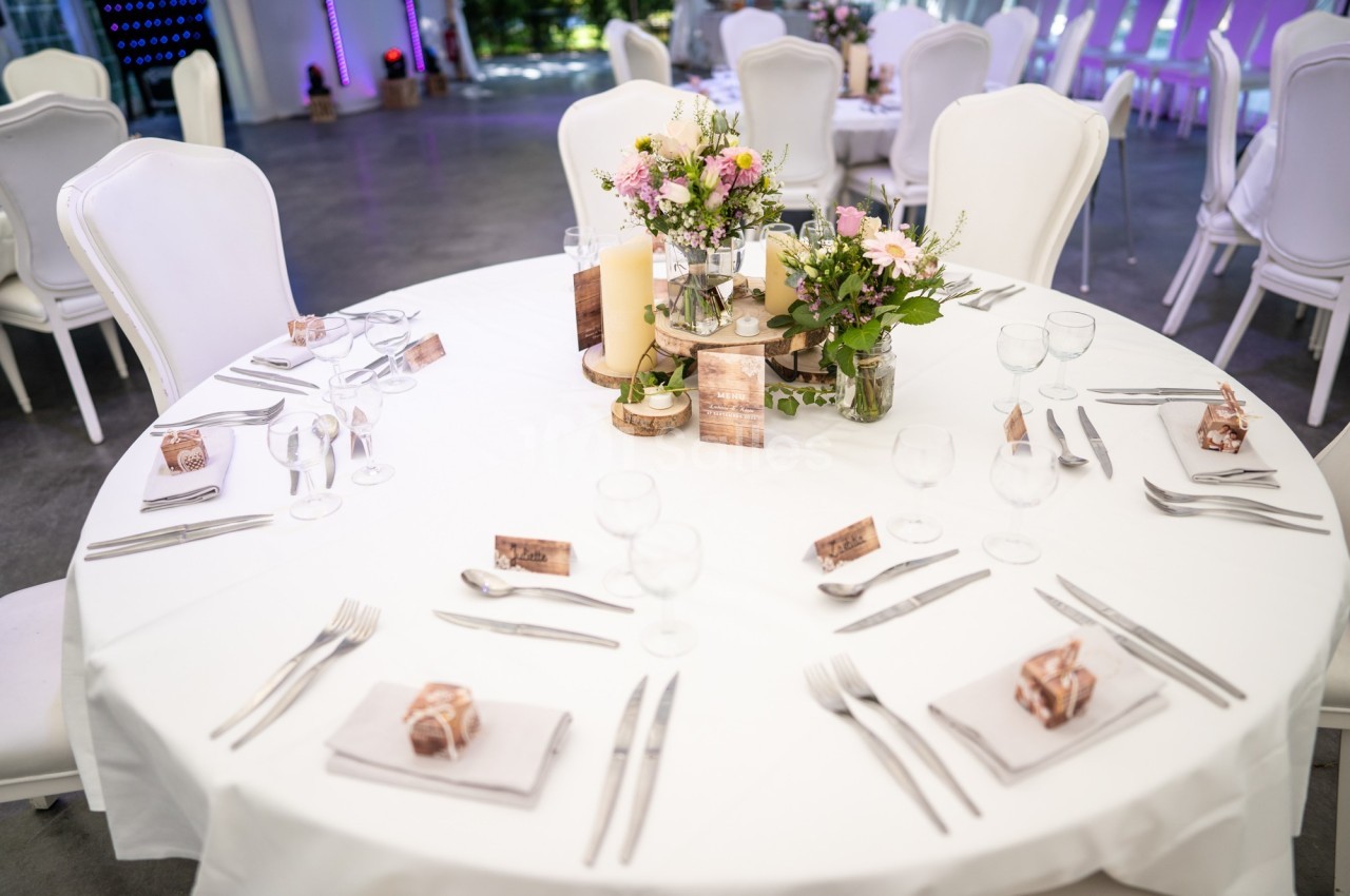 Table ronde décorée pour un événement, avec nappes blanches, fleurs, bougies et couverts disposés pour plusieurs convives.