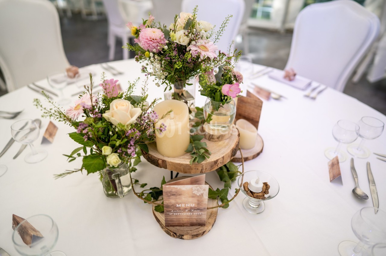 Table décorée pour un événement avec bougies, fleurs fraîches et un menu en bois sur un support en bois.