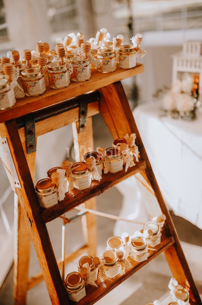 Petits pots de miel disposés sur une échelle en bois, décorée pour un événement festif ou un mariage.