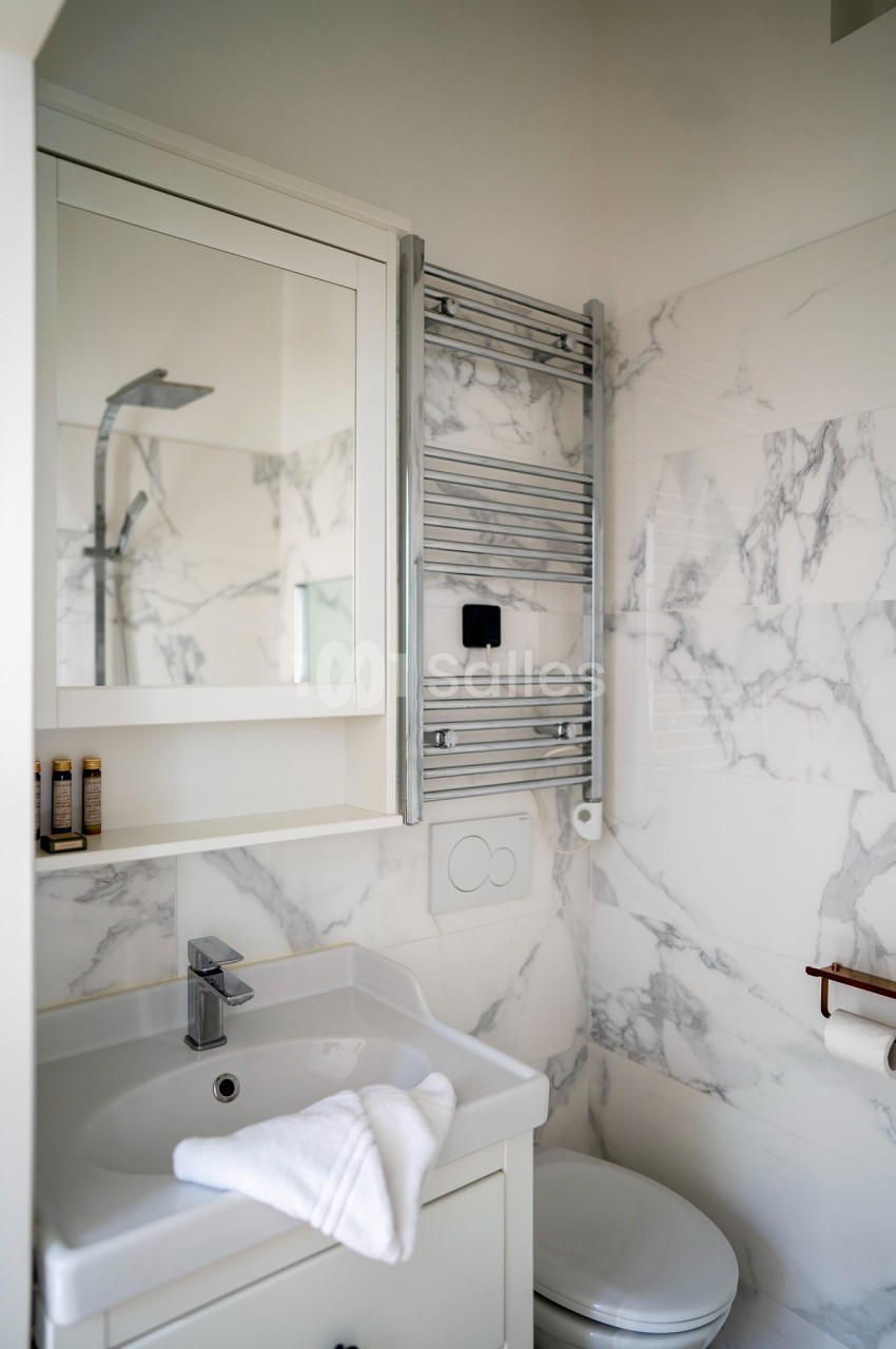 Salle de bain moderne avec lavabo, miroir, sèche-serviettes mural, douche et carrelage effet marbre.