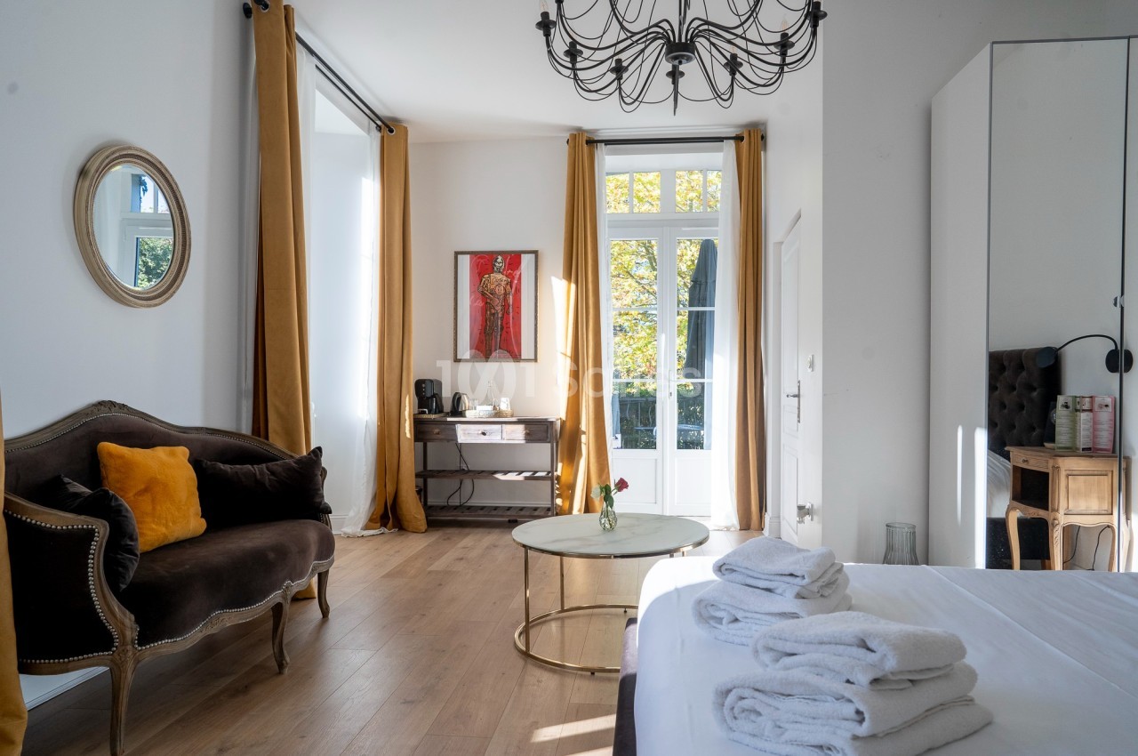 Chambre lumineuse avec lit, canapé, bureau, table basse et grandes fenêtres encadrées de rideaux jaunes.