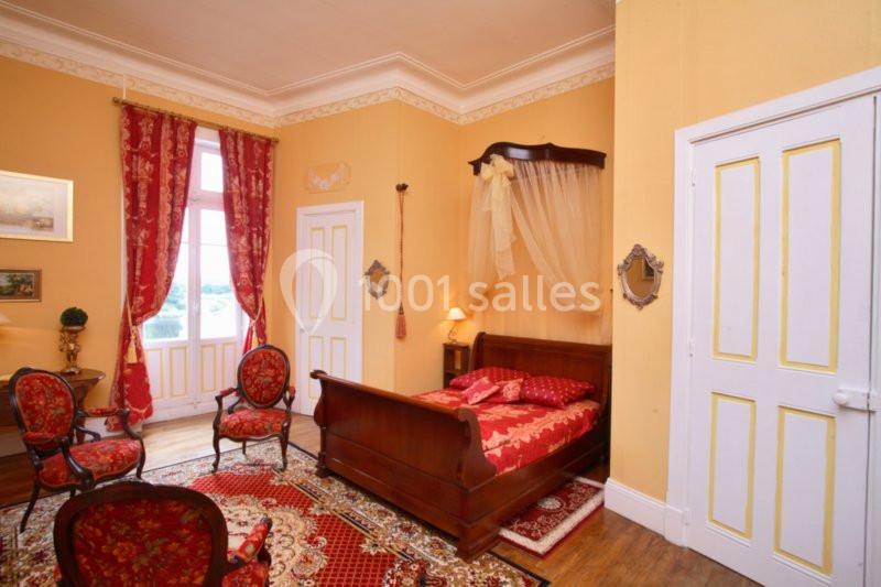 Chambre classique avec lit à baldaquin, meubles anciens, murs jaunes et rideaux rouges, éclairée par une fenêtre.