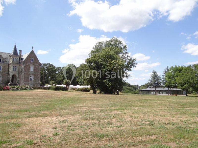 Grand espace herbeux avec un bâtiment en pierre à gauche, des arbres et une structure couverte à droite sous un ciel dégagé.