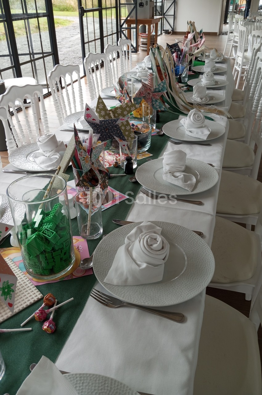 Table dressée pour un événement, avec nappes blanches, serviettes pliées, couverts et décorations colorées.