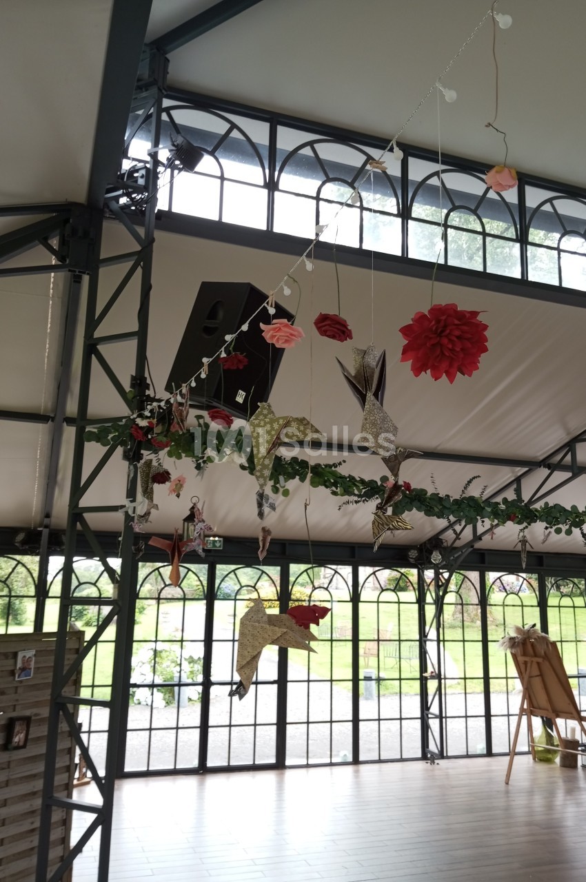 Décorations suspendues en papier et tissu, représentant des oiseaux et des fleurs, dans une salle lumineuse avec verrières.