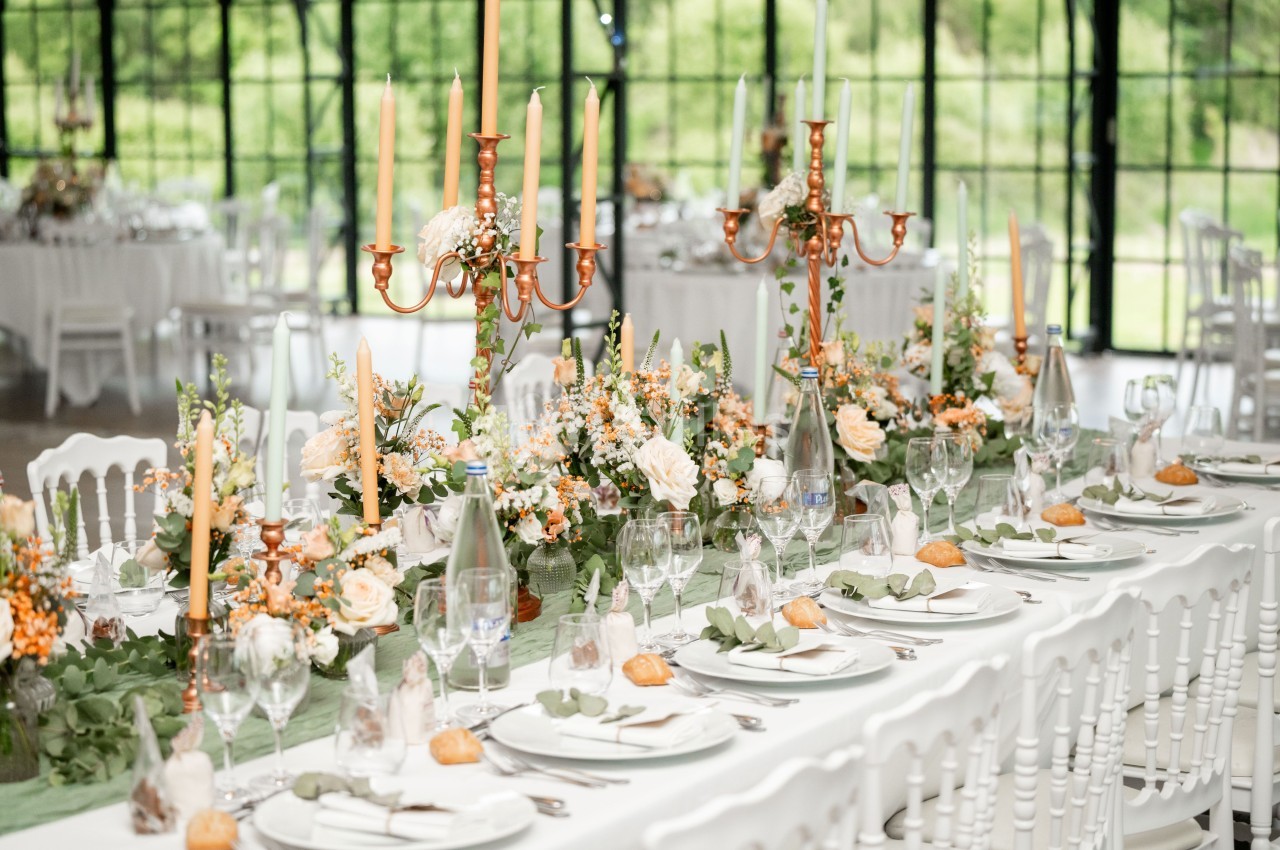 Table de réception élégamment dressée avec chandeliers dorés, fleurs fraîches et vaisselle raffinée dans une salle lumineuse.