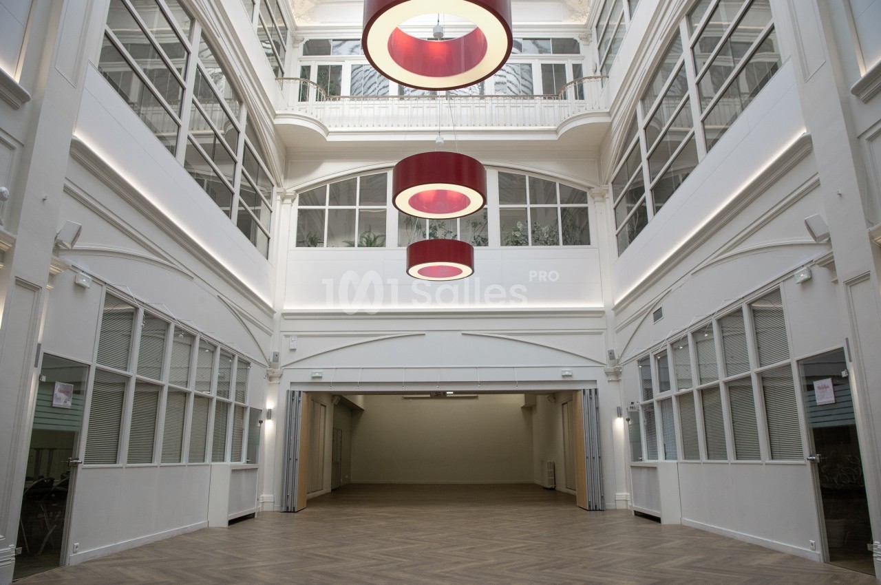 Vue intérieure d'une grande salle lumineuse avec parquet, verrière et suspensions rouges circulaires.