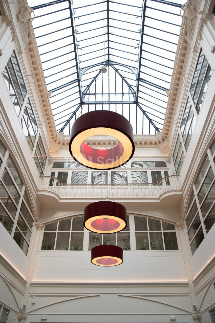 Plafond vitré d'une galerie lumineuse avec trois grands luminaires circulaires suspendus.
