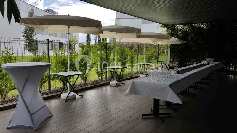 Terrasse aménagée avec des tables hautes, des parasols et une table dressée pour un événement en extérieur.