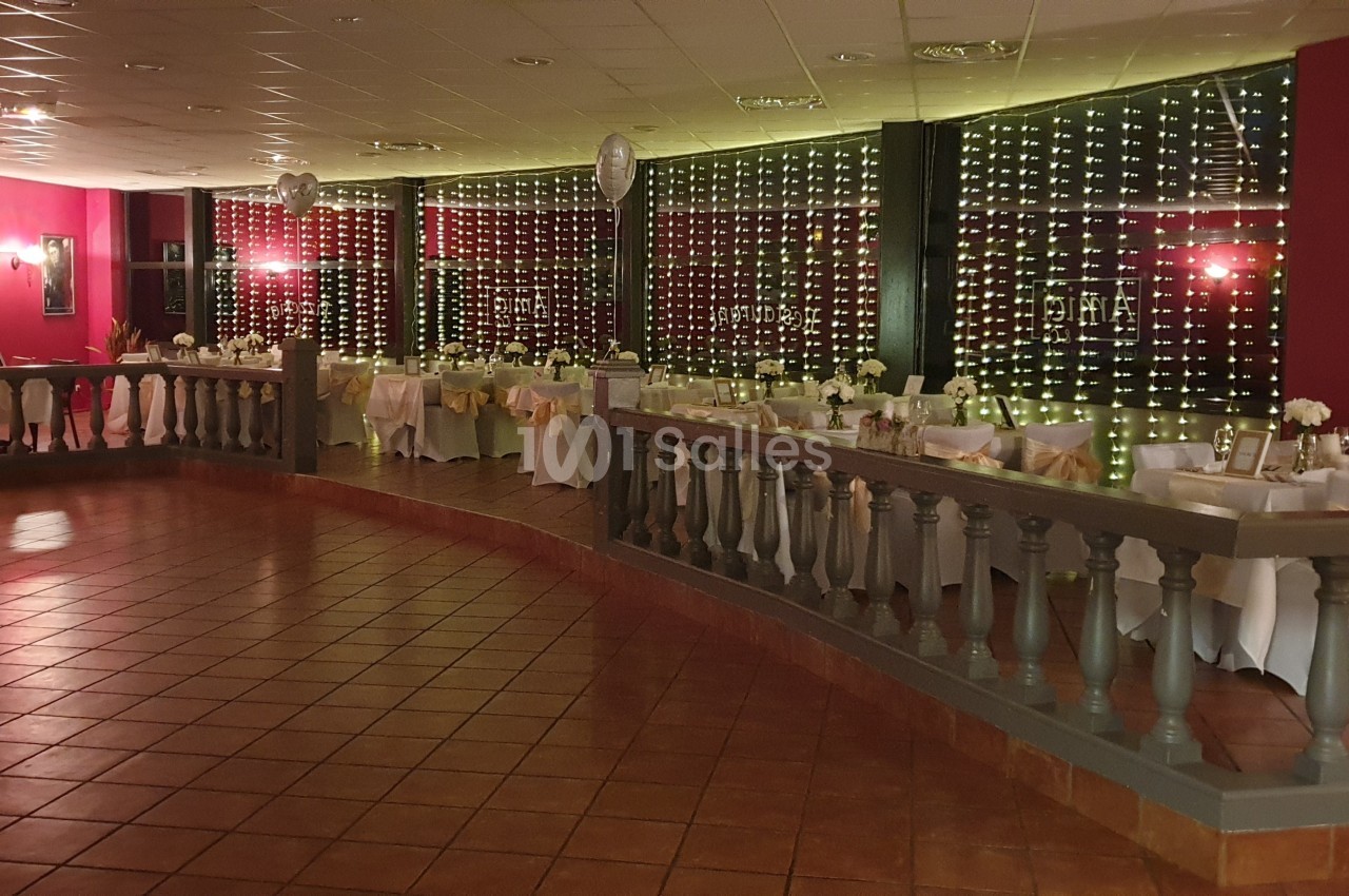 Salle de réception décorée avec des tables dressées, des ballons et un éclairage tamisé.
