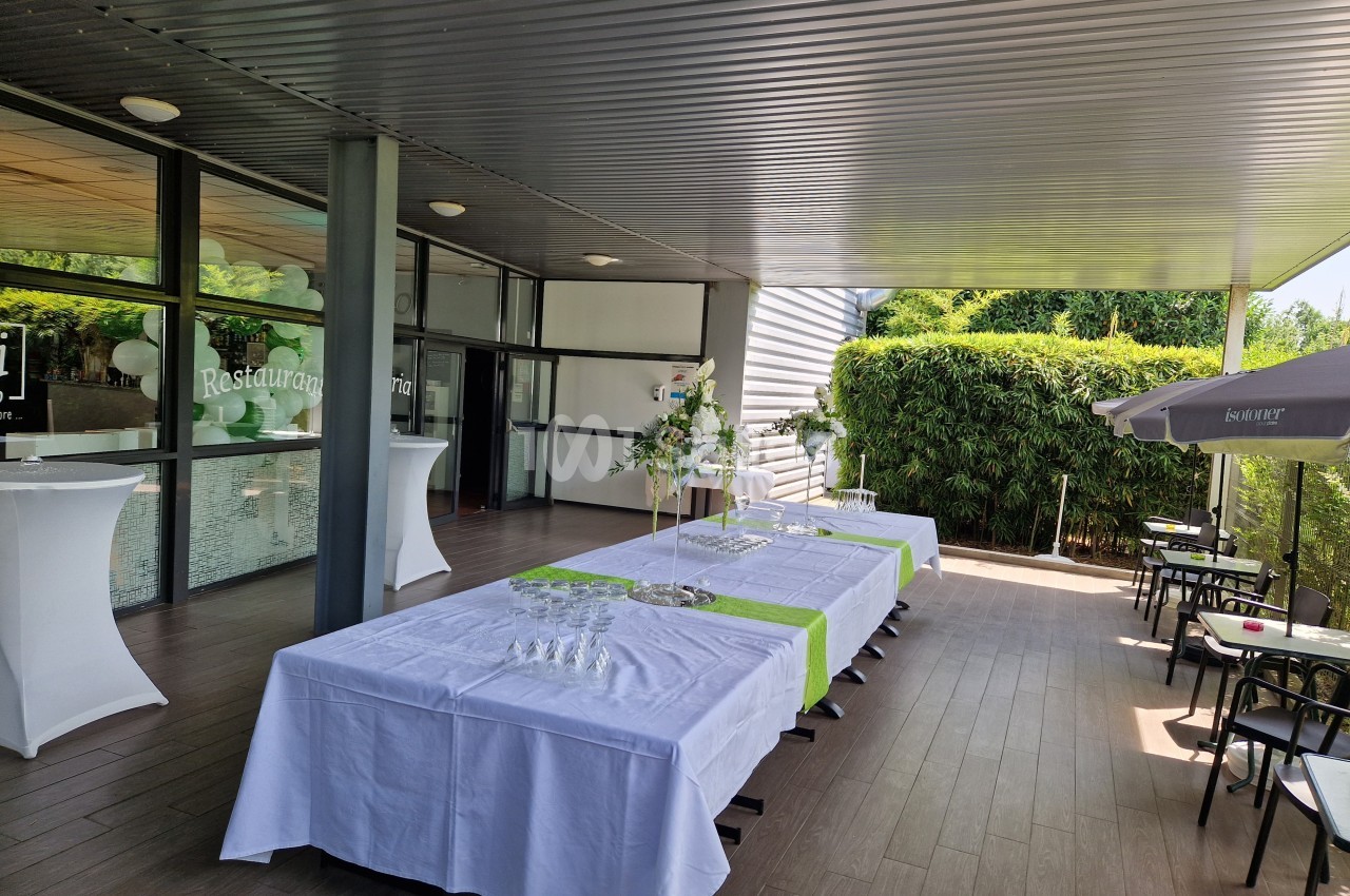 Terrasse couverte avec tables dressées pour un événement, entourée de verdure et équipée de parasols.