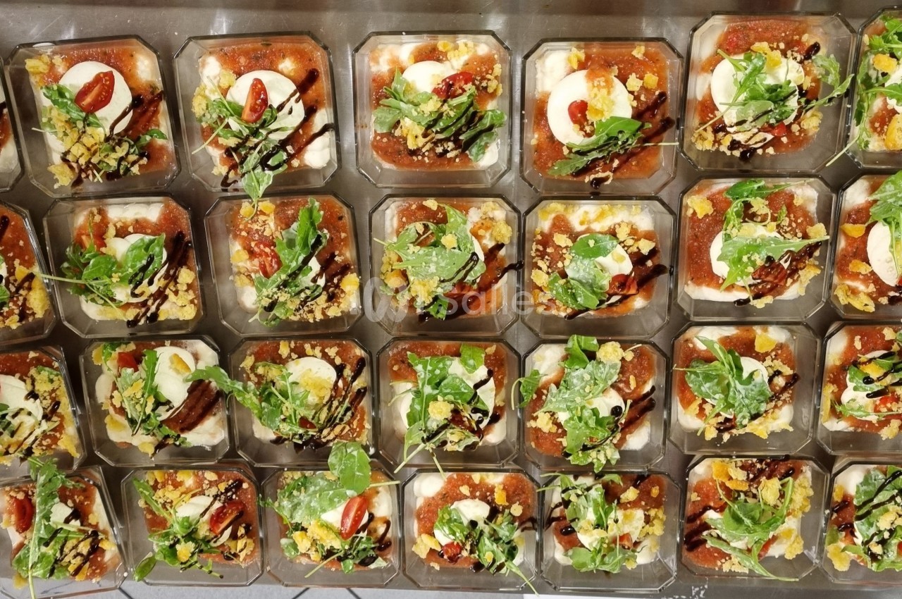 Plateau de verrines garnies de légumes, fromage, roquette et sauce, disposées en rangées sur une table.
