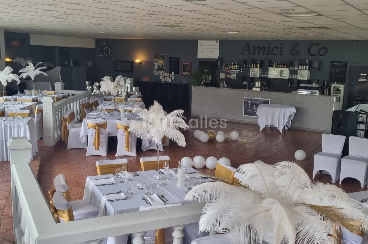 Salle de réception décorée avec des tables dressées, des chaises blanches ornées de rubans dorés et des plumes blanches.