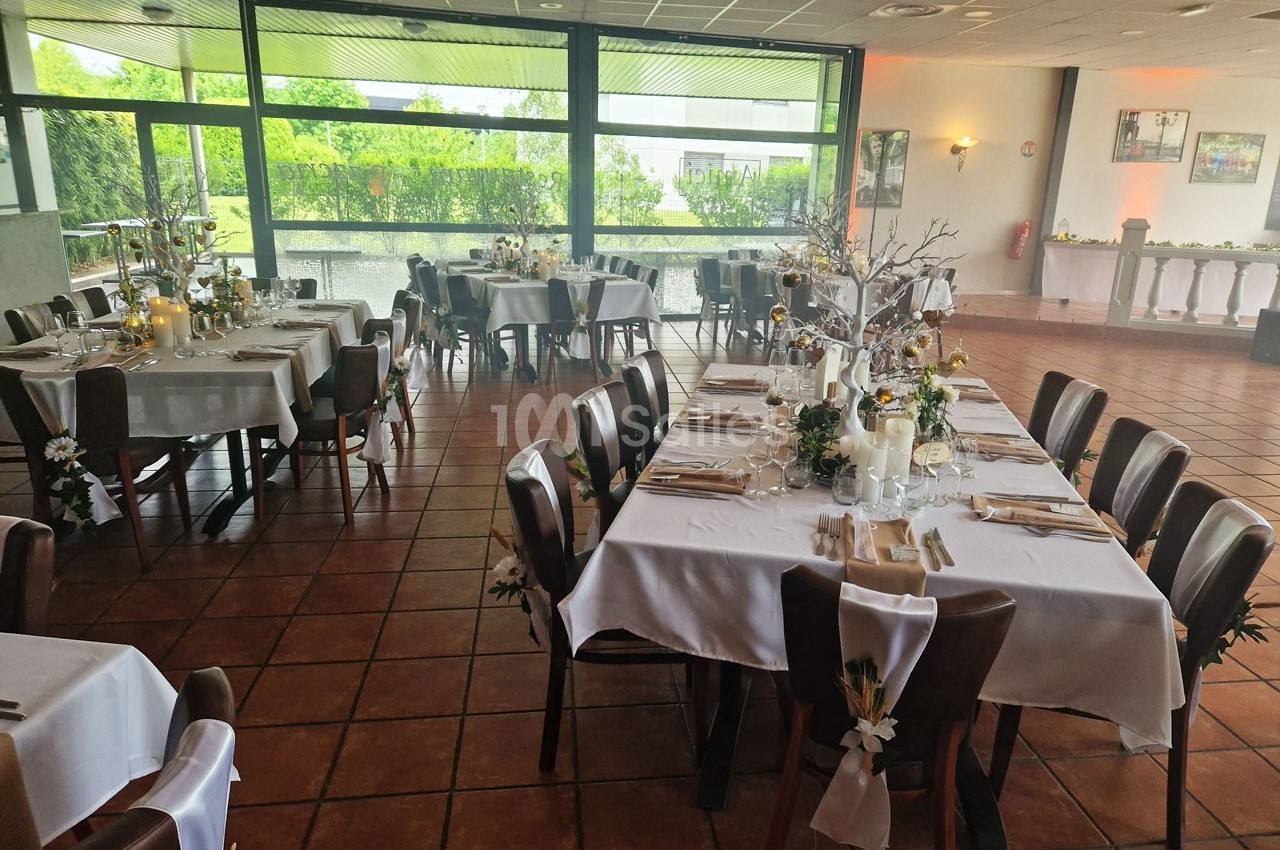 Salle de réception décorée pour un événement, avec des tables dressées, nappes blanches et arrangements floraux.