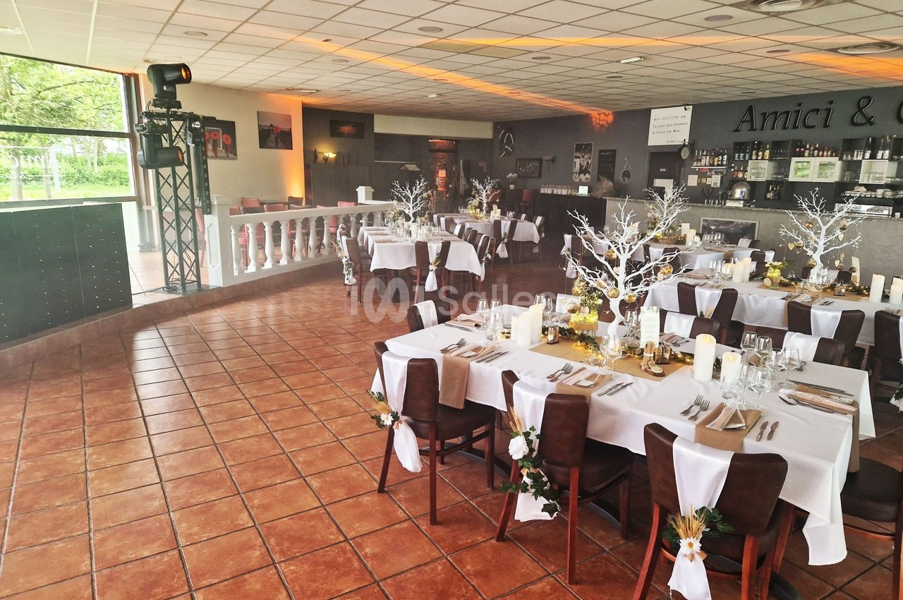 Salle de réception décorée pour un événement, avec tables dressées, chaises ornées et arbres lumineux en centre de table.