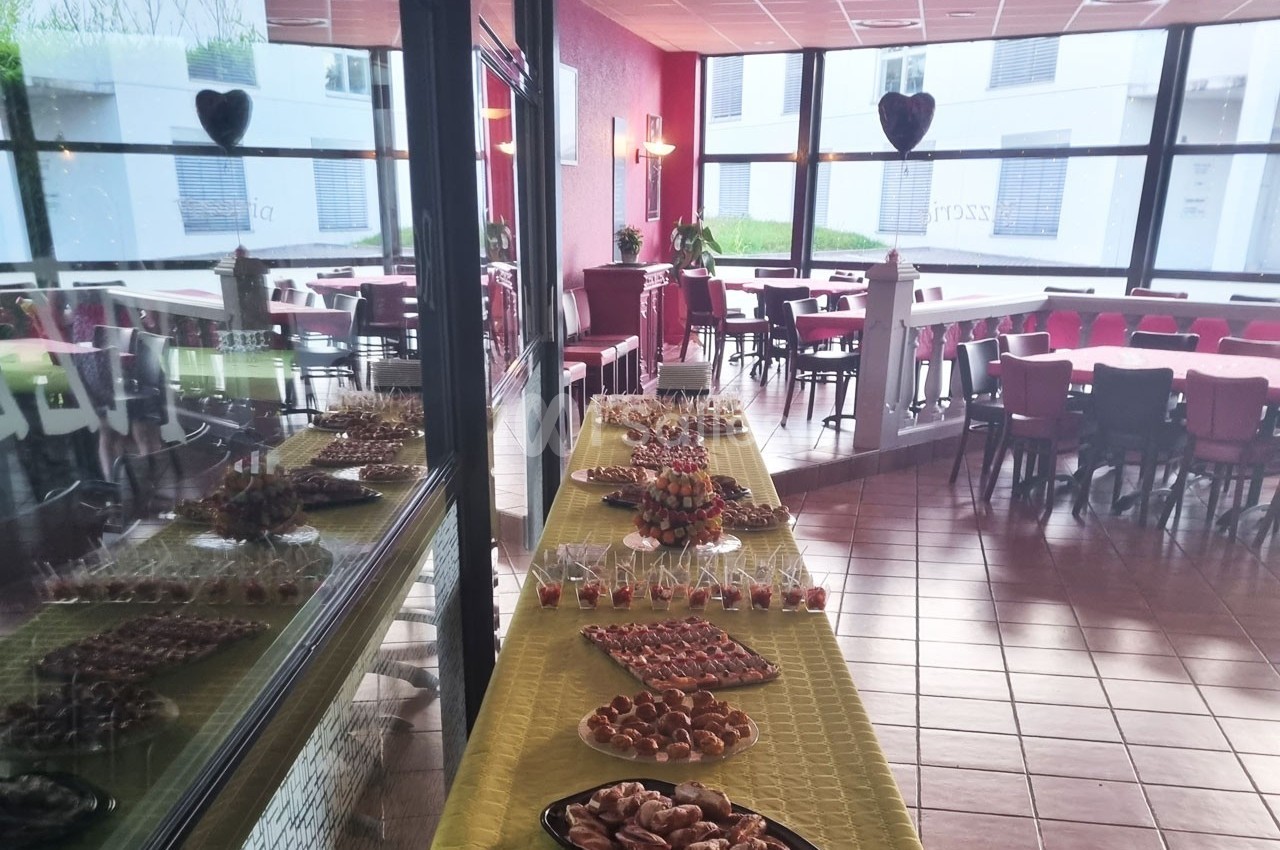 Buffet dressé avec des amuse-bouches et viennoiseries dans une salle lumineuse avec tables et chaises rouges.