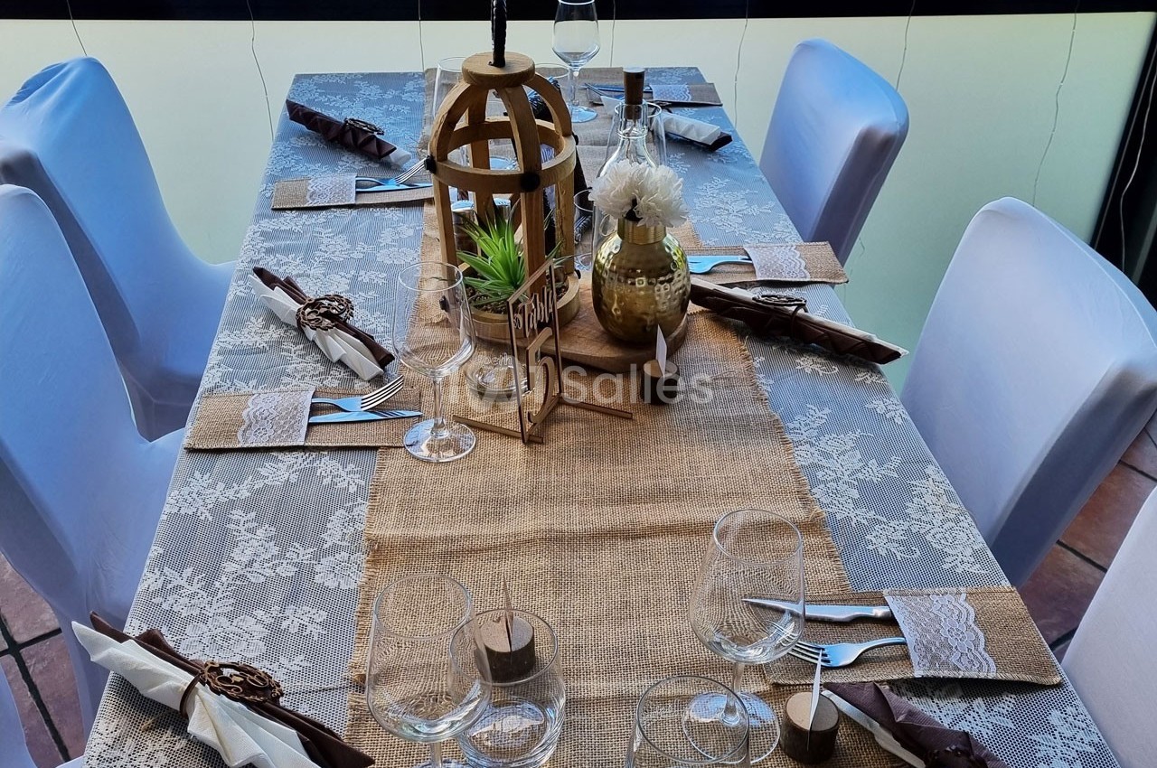 Table dressée avec une nappe en toile de jute, décorations rustiques, vaisselle et serviettes soigneusement disposées.