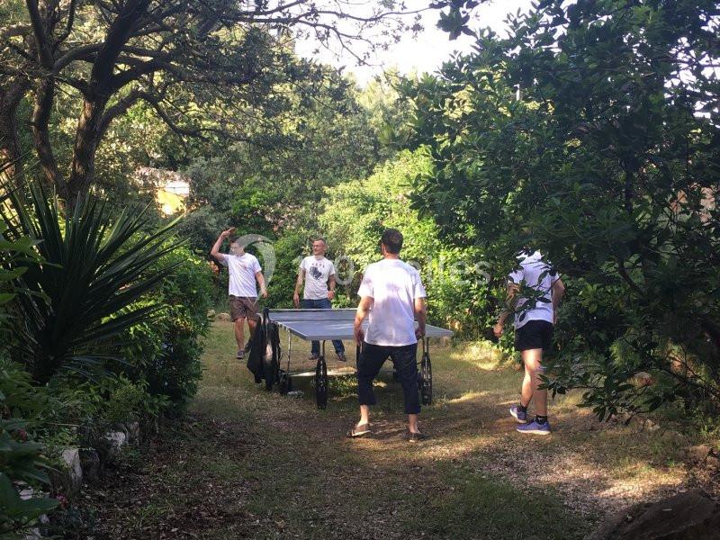 Quatre personnes transportent une table de ping-pong à travers un chemin entouré de végétation dense.