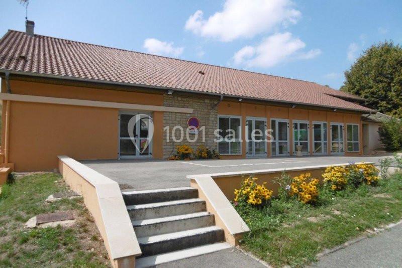 Bâtiment à un étage avec façade beige, toit en tuiles, escaliers d'accès et parterre de fleurs jaunes.