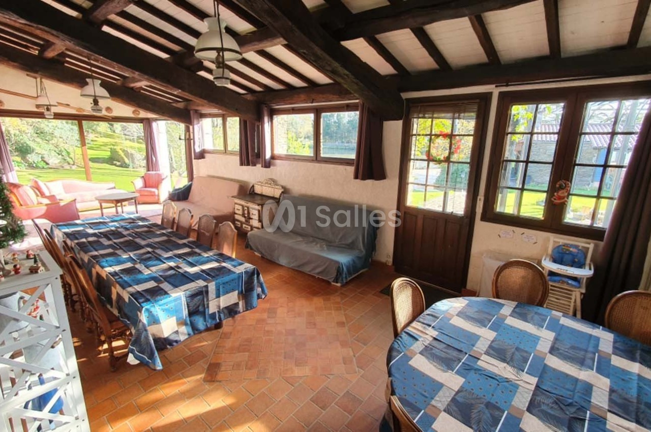 Salle à manger lumineuse avec grandes fenêtres, tables recouvertes de nappes bleues et vue sur un jardin verdoyant.