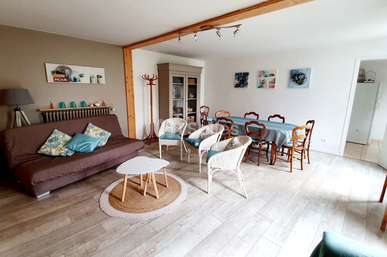 Salon lumineux avec canapé, table à manger, chaises en bois, meubles de rangement et décoration murale colorée.