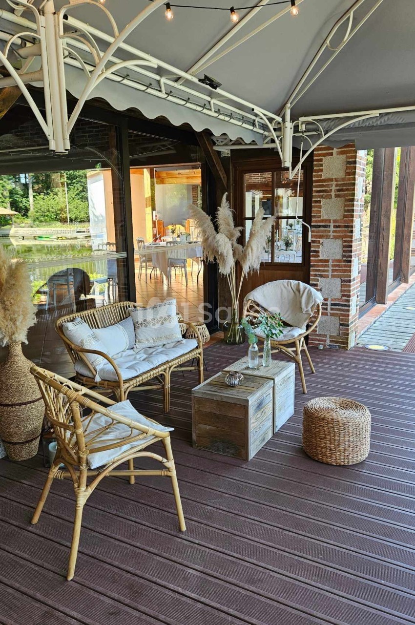 Terrasse aménagée avec mobilier en rotin, table basse en bois, plantes décoratives et guirlande lumineuse suspendue.