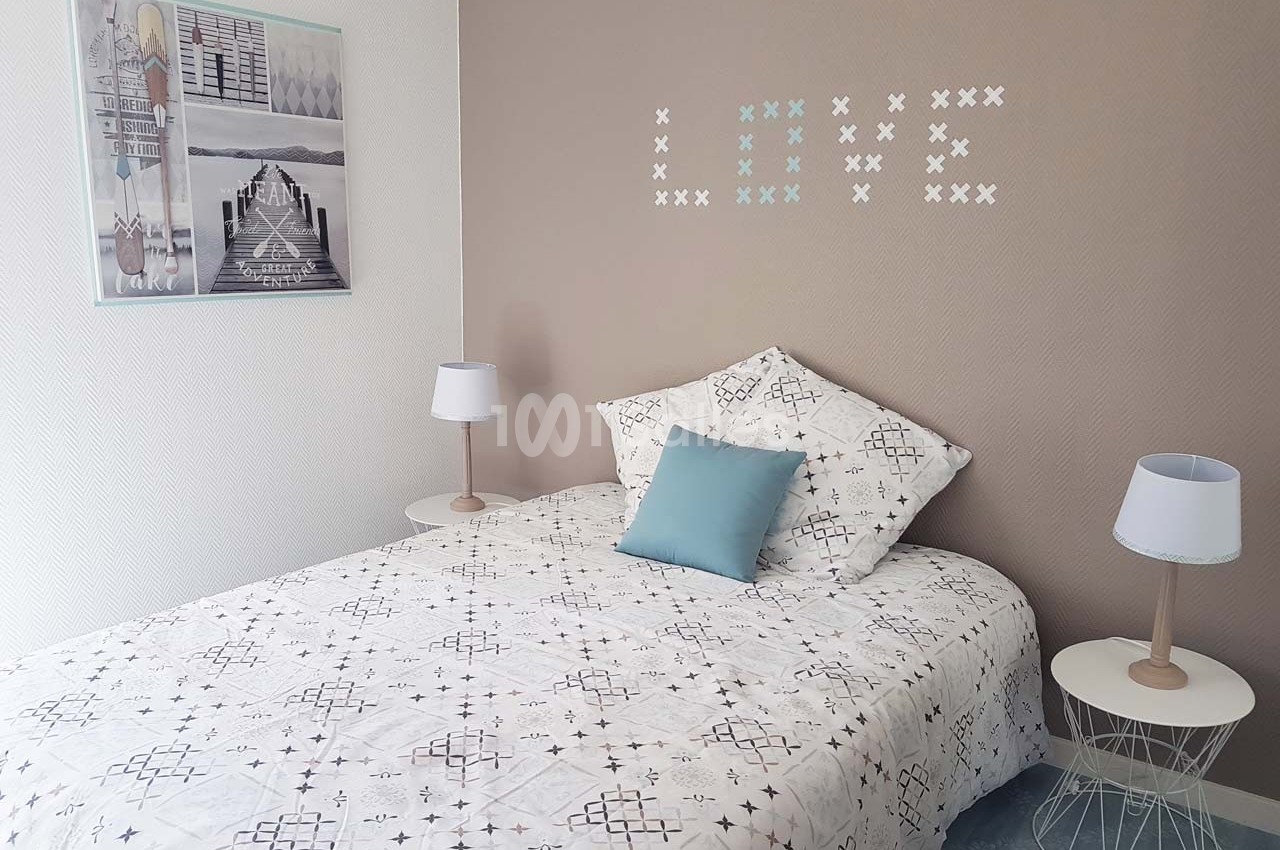 Chambre lumineuse avec un lit simple, une décoration murale ’LOVE’ et deux tables de chevet avec lampes.