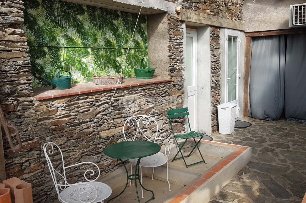 Petite cour en pierre avec mobilier de jardin en métal, mur en pierre, plantes et porte blanche.