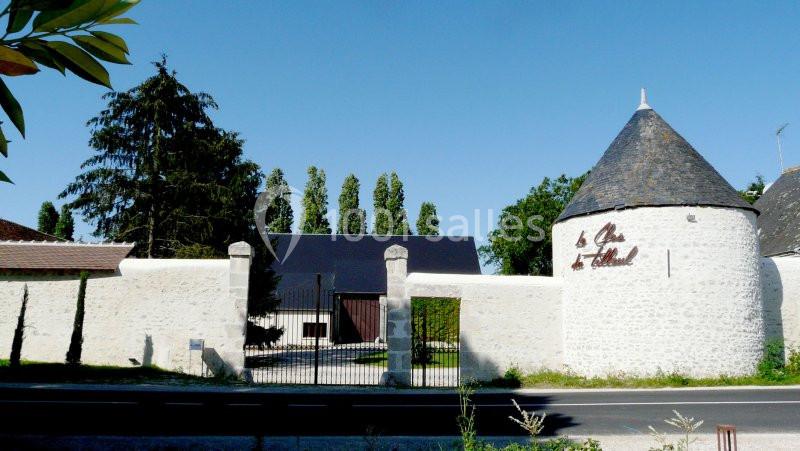 Façade d'un domaine viticole avec un mur en pierre blanche, une tour conique et une entrée grillagée.