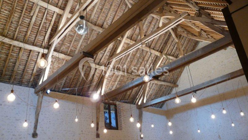 Plafond en bois avec poutres apparentes, éclairé par des ampoules suspendues dans une pièce aux murs clairs.