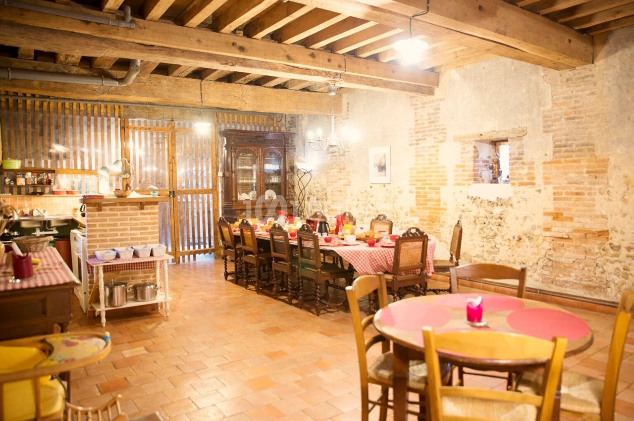 Salle à manger rustique avec tables en bois, nappes à carreaux rouges, murs en pierre et plafond avec poutres apparentes.