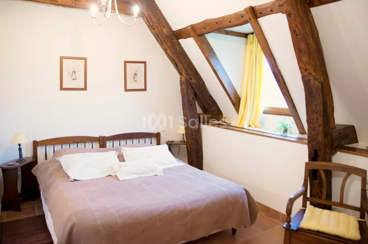 Chambre lumineuse avec poutres apparentes, lit double, fenêtres avec rideaux jaunes et décoration sobre.