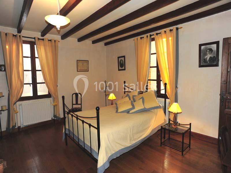 Chambre avec lit double en fer forgé, parquet en bois, rideaux jaunes et poutres apparentes au plafond.