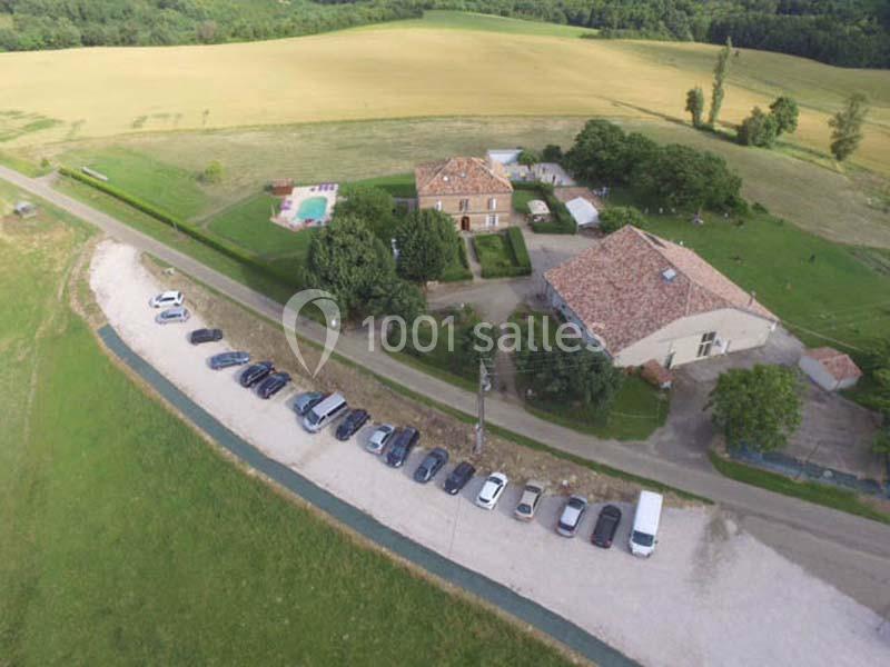 Vue aérienne d'un domaine rural avec bâtiments, piscine, espaces verts et voitures stationnées le long d'une route.