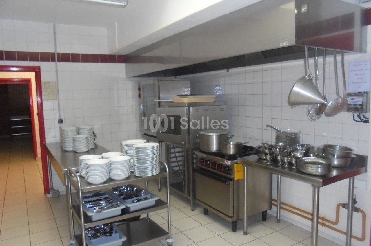 Cuisine professionnelle équipée avec four, plaques de cuisson, ustensiles suspendus et chariots contenant assiettes et…