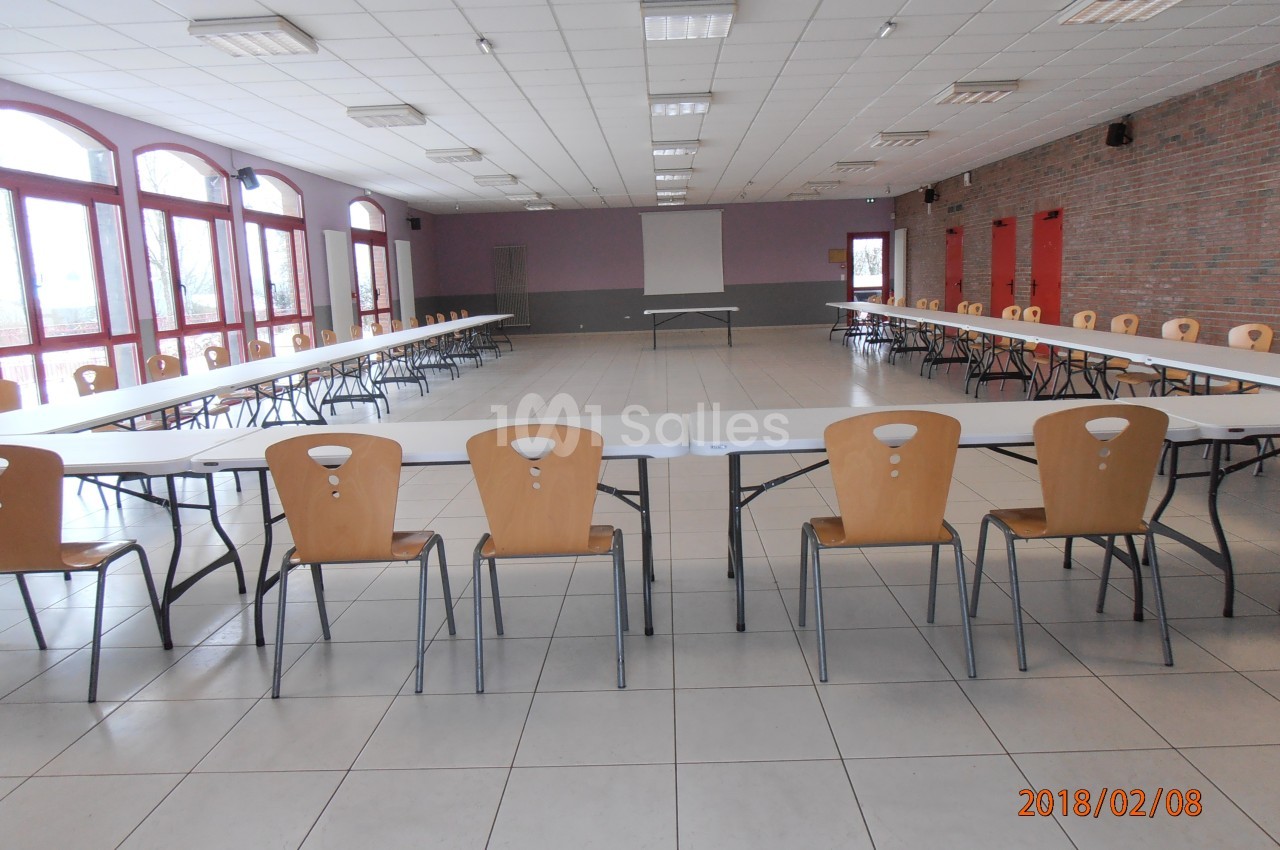 Salle de réunion vide avec tables disposées en U, chaises en bois, murs en briques et grandes fenêtres laissant entrer la…