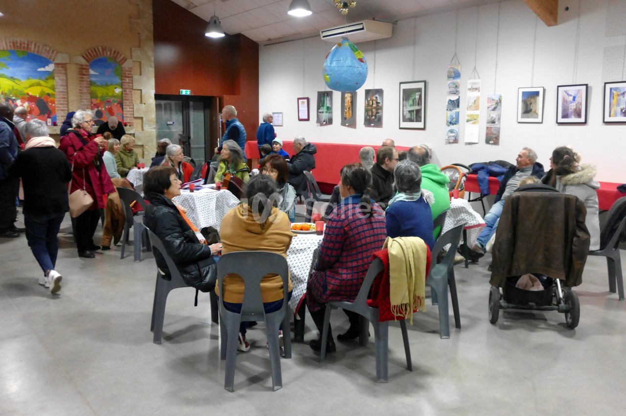 Des personnes assises et debout discutent dans une salle conviviale avec des tables, des chaises et des décorations murales.