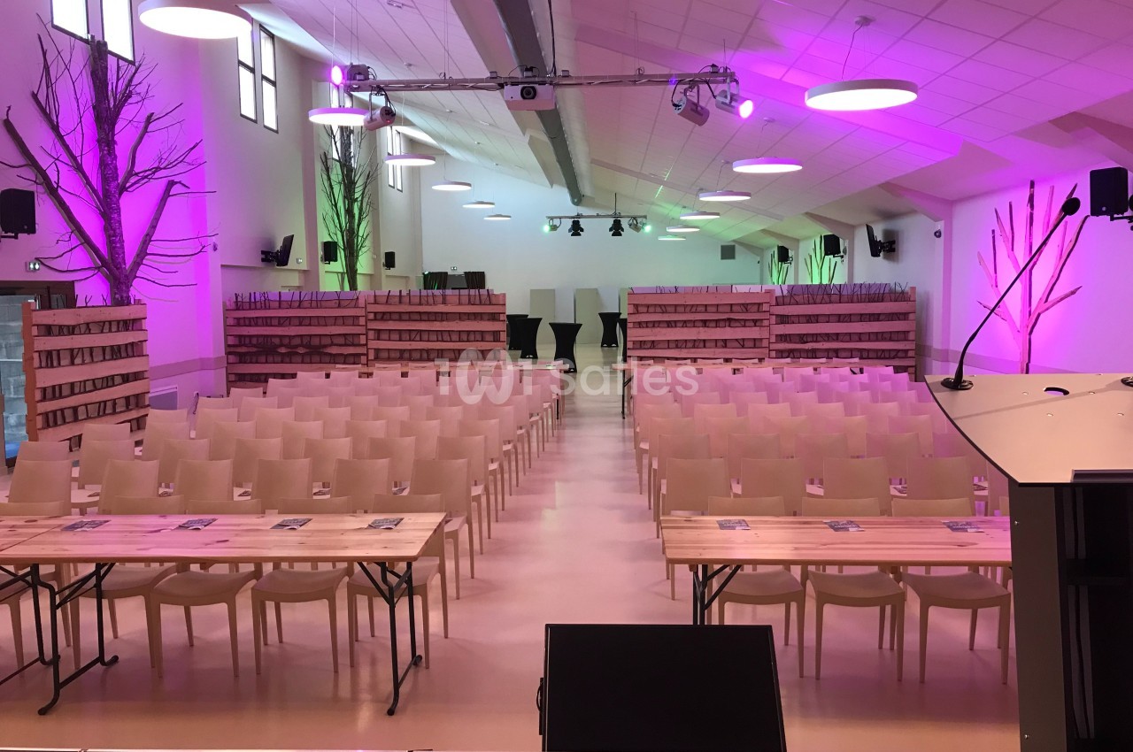 Salle de conférence aménagée avec des rangées de chaises, des tables et un éclairage coloré rose et vert.