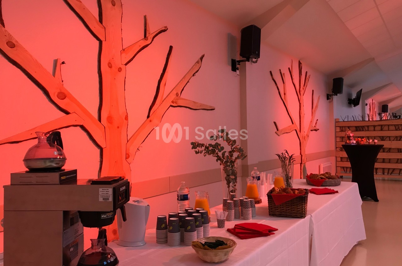 Table de buffet avec boissons, tasses et décorations naturelles dans une salle éclairée par une lumière rouge.