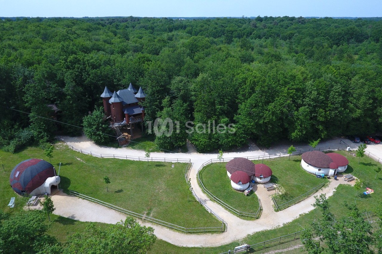 Vue aérienne d'un domaine forestier avec des cabanes rondes, un bâtiment en forme de château et des chemins sinueux.