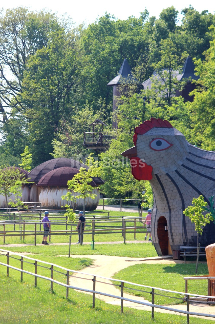 Parc avec des structures en forme de poule et de champignons, entouré de verdure et de visiteurs se promenant.