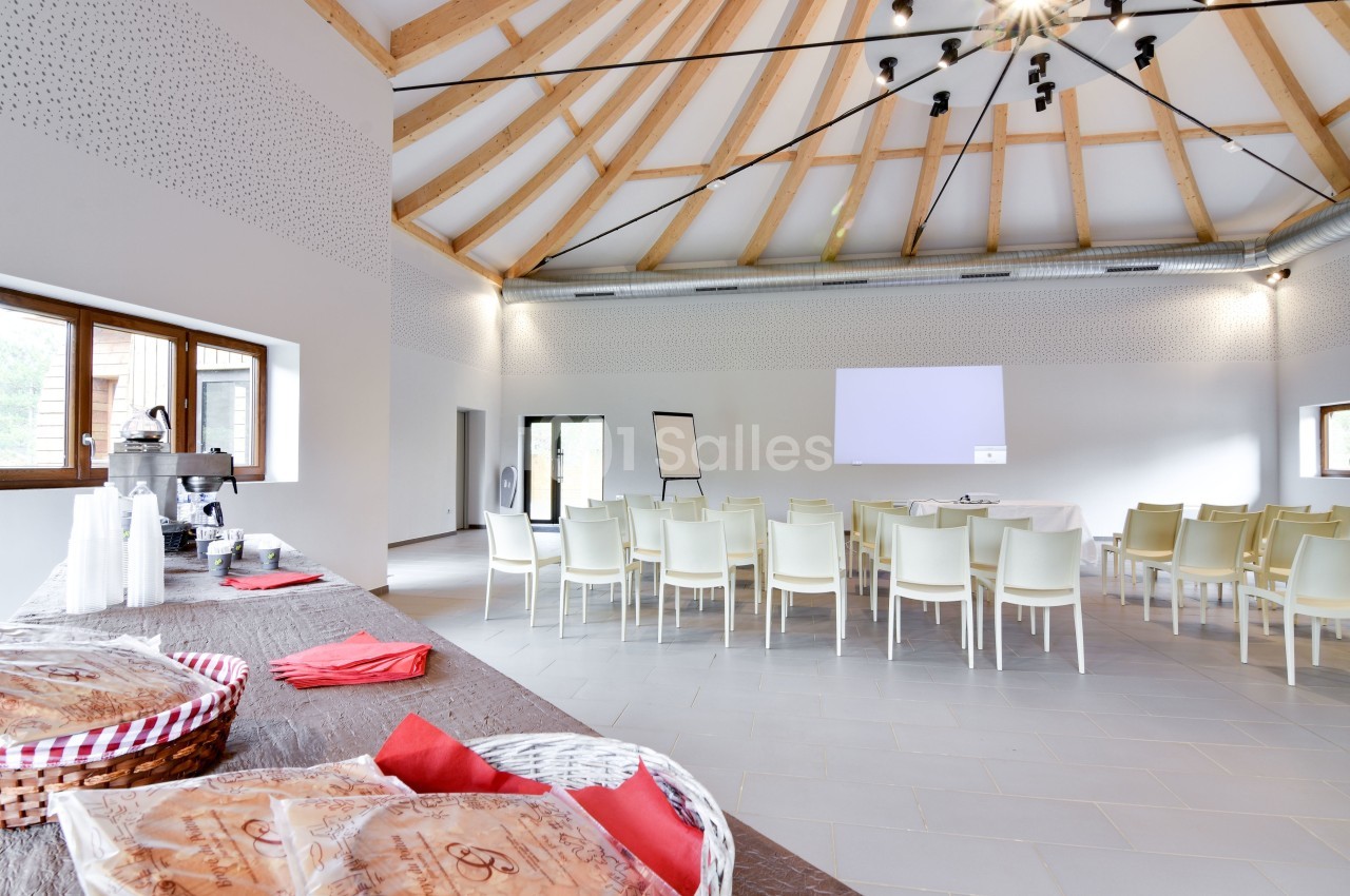 Salle lumineuse avec des chaises disposées face à un écran de projection, table avec collations au premier plan.