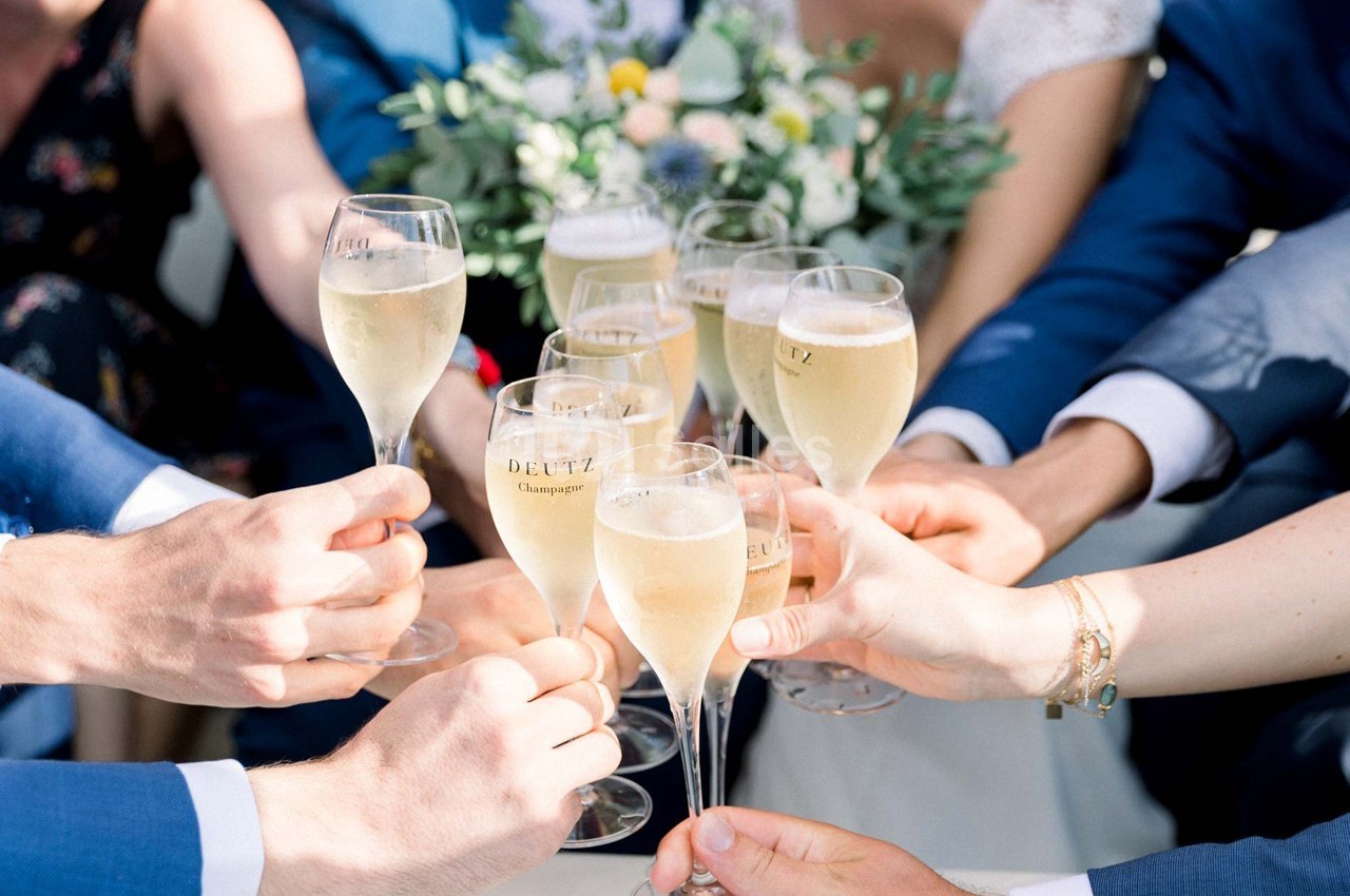 Des mains trinquent avec des coupes de champagne devant un bouquet de fleurs.