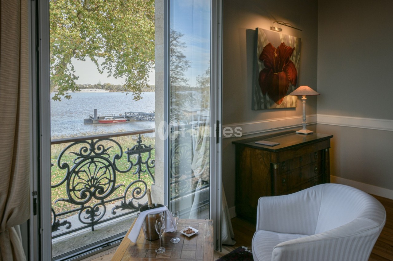 Vue depuis un salon élégant avec fauteuil, table basse et balcon donnant sur une rivière bordée d'arbres.