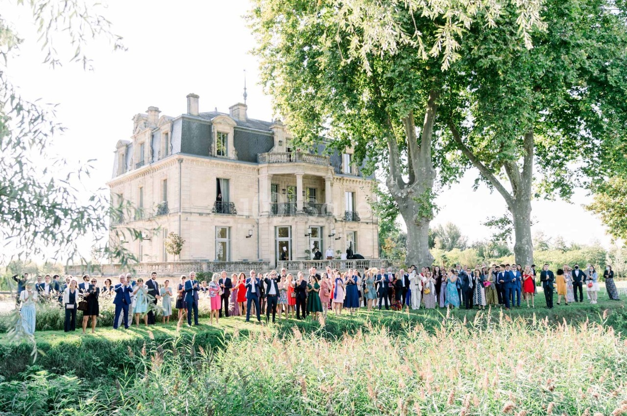 Groupe de personnes posant devant un grand château entouré de verdure par une journée ensoleillée.