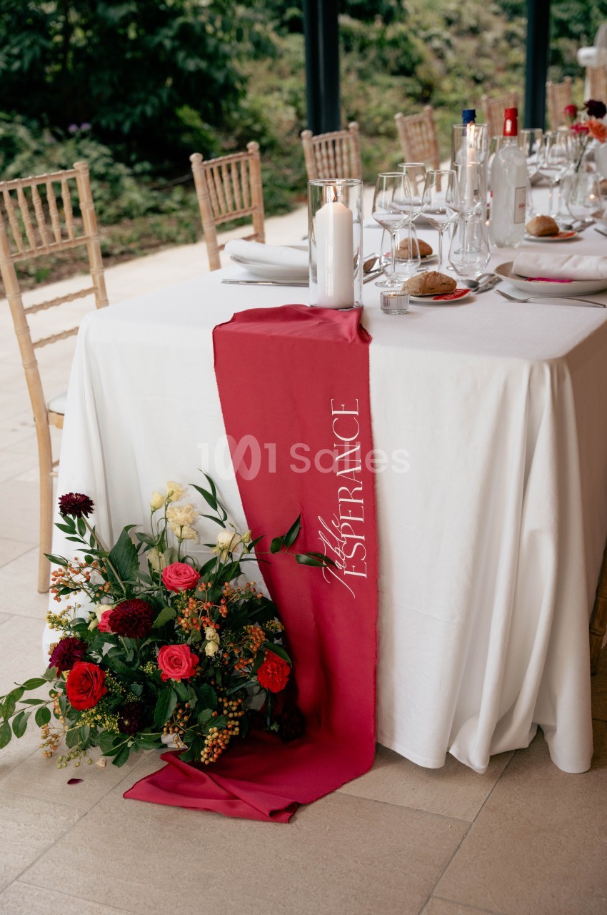 Table décorée avec une nappe blanche, un chemin de table rouge, des fleurs colorées et des couverts élégants.